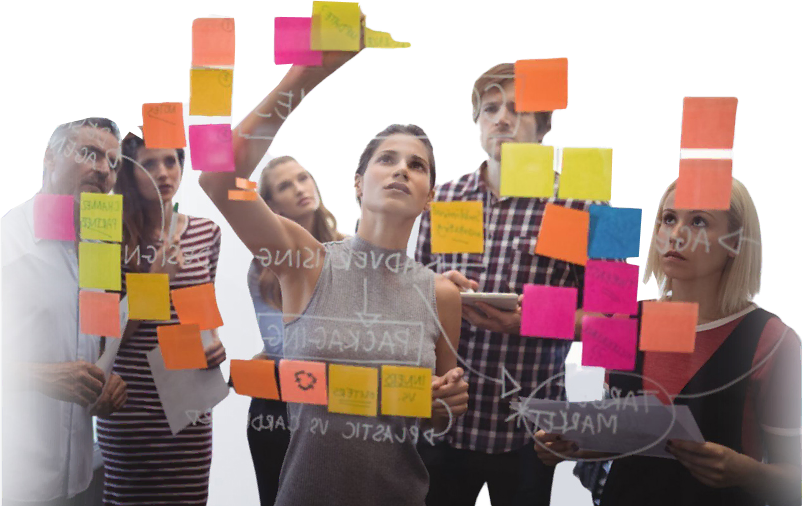 Group of people collaborating with sticky notes on a glass wall in a workspace.